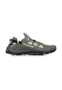 Salomon outdoor shoe in dark gray with beige accents. Features a rubber sole, mesh panels, and a rear strap with red detailing. Lightweight design.