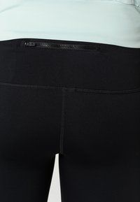 Černé legíny s kapsou na zip v pase, bezproblémovým švem a hladkým, elastickým materiálem.