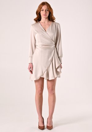 Helles beige Wickelkleid mit langen Ärmeln, einem V-Ausschnitt und einem fließenden, gestuften Rock. Glatte Textur, eleganter Fall, kombiniert mit braunen Absätzen.