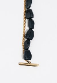 Pulsera de piedra negra que presenta cuentas de forma irregular y una cadena en tono dorado, terminada con un cierre de palanca horizontal.