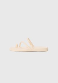 Beige flip-flop sandal with two thin straps and a toe loop, made of soft rubber material, featuring a smooth texture and a flat sole.
