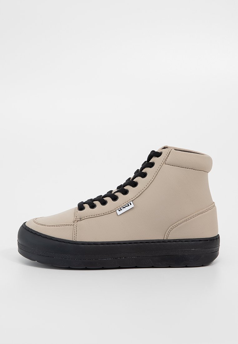Beige High-Top-Sneaker mit schwarzer Gummisohle und Schnürsenkeln. Glattes synthetisches Material mit Nahtdetails und einem Logostick auf der Seite.