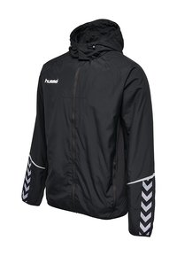 Veste à capuche zippée noire avec logo hummel blanc sur la poitrine et motifs en chevron blancs sur les manches, légère et conçue pour les activités en extérieur.