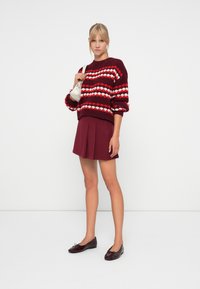 Maroon knitted sweater with red and white patterns, paired with a matching pleated maroon skirt. Black patent ballet flats and white bag.
