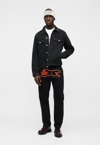 Μαύρο τζιν μπουφάν με εμπρόσθιες τσέπες, μαύρο παντελόνι φόρμας με κόκκινο καρτούν κουνέλι και μαύρα παπούτσια. Λευκό μπλουζάκι και πλεκτός σκούφος.