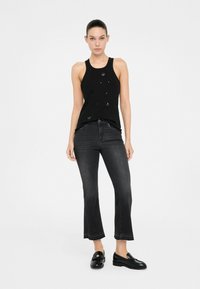 Top negro sin mangas con sutil detalle de lentejuelas, combinado con unos vaqueros acampanados de color gris oscuro. Los zapatos son mocasines negros con un tacón bajo.