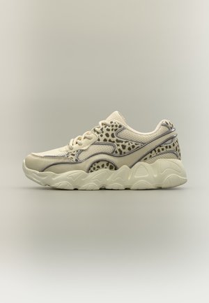 Beige sneaker met golvende zool, mesh- en suède panelen, en een donker gevlekt patroon op het bovenwerk, zijaanzicht tegen een effen achtergrond.