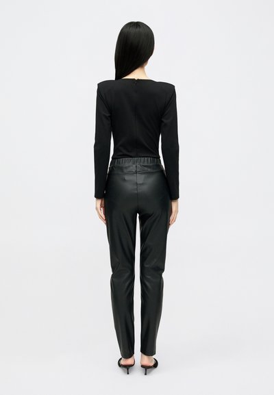 Μαύρο μπλουζάκι με μακριά μανίκια, στρογγυλή λαιμόκοψη και φερμουάρ στην πλάτη, συνδυασμένο με στενά μαύρα δερμάτινα παντελόνια που διαθέτουν ψηλή ελαστική μέση.