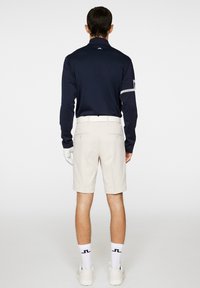 Granatowa koszulka polo z długim rękawem i beżowe szorty. Koszulka polo posiada stójkę oraz paski na rękawach. Model nosi białe skarpetki i buty.