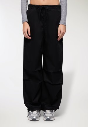Pantaloni cargo neri, morbidi e larghi, con vita regolabile tramite cordoncino, due tasche laterali e polsini elastici, realizzati in materiale leggero e liscio.