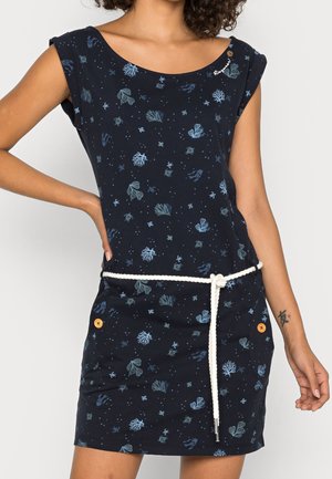 Granatowa sukienka z niebieskimi nadrukami morskich stworzeń, krótkimi rękawami, białym sznurowym paskiem zawiązanym w talii oraz pomarańczowymi guzikami na kieszeniach, noszona przez osobę z tatuażem na ramieniu.