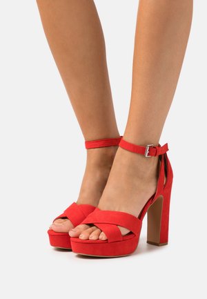 Sandales compensées en daim rouge avec des brides croisées et une bride de cheville à boucle, dotées d'un talon bloc haut et d'un design à bout ouvert.