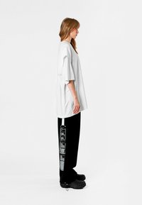 Camiseta blanca de gran tamaño con mangas cortas, combinada con pantalones negros que presentan un estampado gráfico y una franja de tela de acento. Calzado negro texturizado.