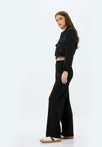 Chaqueta negra corta con botones a presión, combinada con pantalones negros holgados y zapatillas blancas con rayas negras. Diseño simple y casual, sin patrones.