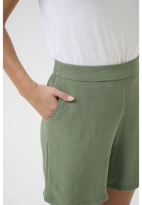 Gröna krinklade tyggshorts med bred midja och sidofickor, tillsammans med en vit kortärmad topp.