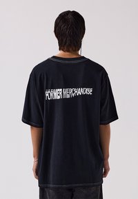 Black oversized t-shirt with short sleeves, featuring white text "FÖRMER MERCHANDISE" across the back, and contrasting stitching.