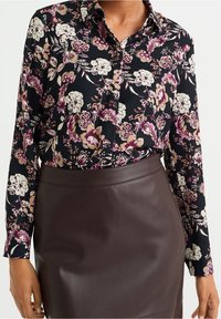 Svart blommig blus med långa ärmar, med rosa och vita blommor, kombinerad med en mörkbrun läderkjol. Mjuk textur över hela plagget.