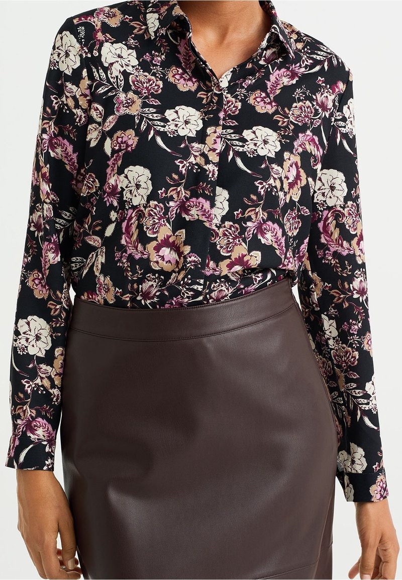 Svart blommig blus med långa ärmar, med rosa och vita blommor, kombinerad med en mörkbrun läderkjol. Mjuk textur över hela plagget.