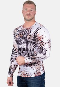 Langarm graphic t-shirt in het wit met een zwart schedel- en kroonontwerp, met ingewikkelde vleugelpatronen en kleurspetters.