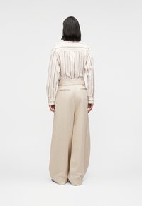 Ελαφρώς ριγέ πουκάμισο σε κρεμ και μπεζ με μανσέτες με κουμπιά, σε συνδυασμό με μπεζ παντελόνια φαρδιάς ίσιας γραμμής, και τα δύο από μαλακό, ρέον ύφασμα.