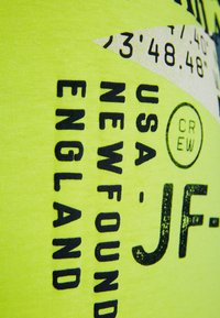 Tejido amarillo brillante con texto y gráficos impresos en negro, que presenta un elemento de diseño diagonal y patrones de letras distintivos.