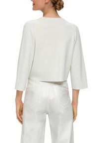 Witte cropped trui met driekwartmouwen, met een gestructureerd uiterlijk. Gecombineerd met witte high-waisted denim broek met achterzakken.