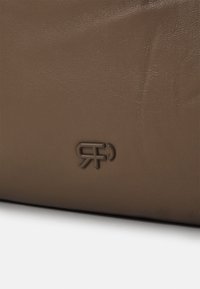 Surface en cuir brun présentant une texture subtile et un logo embossé. Le design est minimaliste avec des contours lisses et aucun matériel visible.