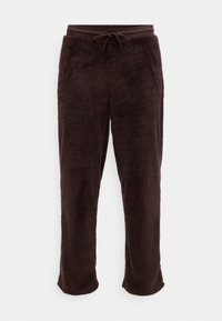 Braune Fleece-Jogginghose mit weicher Textur, ausgestattet mit einem elastischen Bund und einer verstellbaren Kordel. Der Saum hat eine leichte Ausbuchtung.