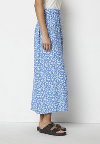 Maxi sukně ve světle modré barvě s bílým květinovým vzorem, vyrobená z měkké tkaniny, s elastickým pasem, v kombinaci s černými sandály.