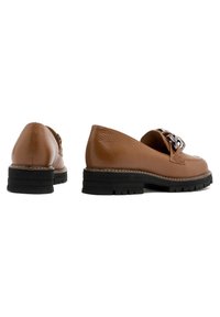 Mocasines de cuero marrón con un acabado texturizado, que presentan una suela negra robusta y un acento decorativo de cadena plateada en la parte delantera.