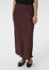 Burgunderfarbener Satin-Maxi-Rock mit glatter Textur, fließendem Schnitt und dezentem Glanz, kombiniert mit schwarzen flachen Schuhen mit Schleifen.