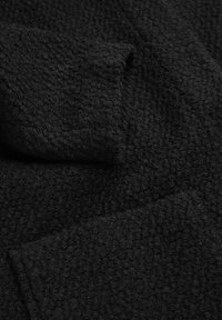 Nahaufnahme eines schwarzen Strickstoffs mit einem strukturierten, gerippten Muster und gewellten Kanten, das das weiche, gemütliche Material hervorhebt.