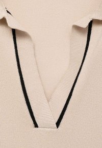 Polo en tricot beige avec un col en V. Présente des rayures noires contrastées le long du col et de la patte de boutonnage. Texture lisse, manches courtes.