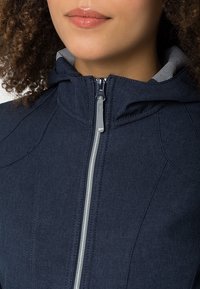 Giacca blu navy con colletto alto e zip frontale. Il tessuto presenta un aspetto testurizzato con dettagli di cucitura visibili.