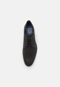 Zapato negro con cordones y parte superior texturizada, que presenta un patrón en zigzag y plantilla azul oscura. Logo de la marca visible en el interior. Suela lisa.