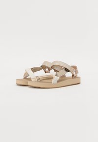 Beige Sandalen mit mehreren Riemen aus gewebtem Textil, einem strukturierten Fußbett und einer flexiblen, strapazierfähigen Sohle. Sie verfügen über ein minimalistische Design.