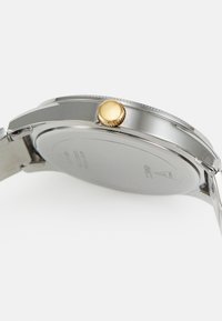 Srebrny zegarek na rękę o polerowanym wykończeniu, z okrągłą kopertą, złoconym koronką i stalową bransoletą. Minimalistyczny design.