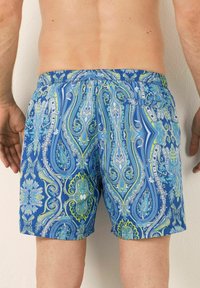 Modré plavky s vzorem paisley v zelené a bílé barvě, se širokým elastickým pasem a zadní kapsou.