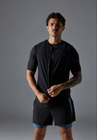 Schwarzes athletisches Zip-Up-Oberteil mit kurzen Ärmeln, kombiniert mit schwarzen Shorts mit blauen Akzenten. Glatte Textur, körperbetonter Schnitt.
