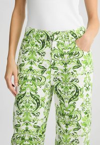 Witte broek met een groen, verfijnd bloemenpatroon; heeft zakken, een knoopsluiting en een elastische tailleband voor comfort.