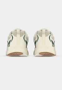 Λευκά αθλητικά παπούτσια με πράσινες λεπτομέρειες, επάνω μέρος από δίχτυ και συνθετικό υλικό, μαξιλαρωμένος γιακάς και ελαστική εξωτερική σόλα με υφή. Σχεδιασμένα για άνεση και ανθεκτικότητα.