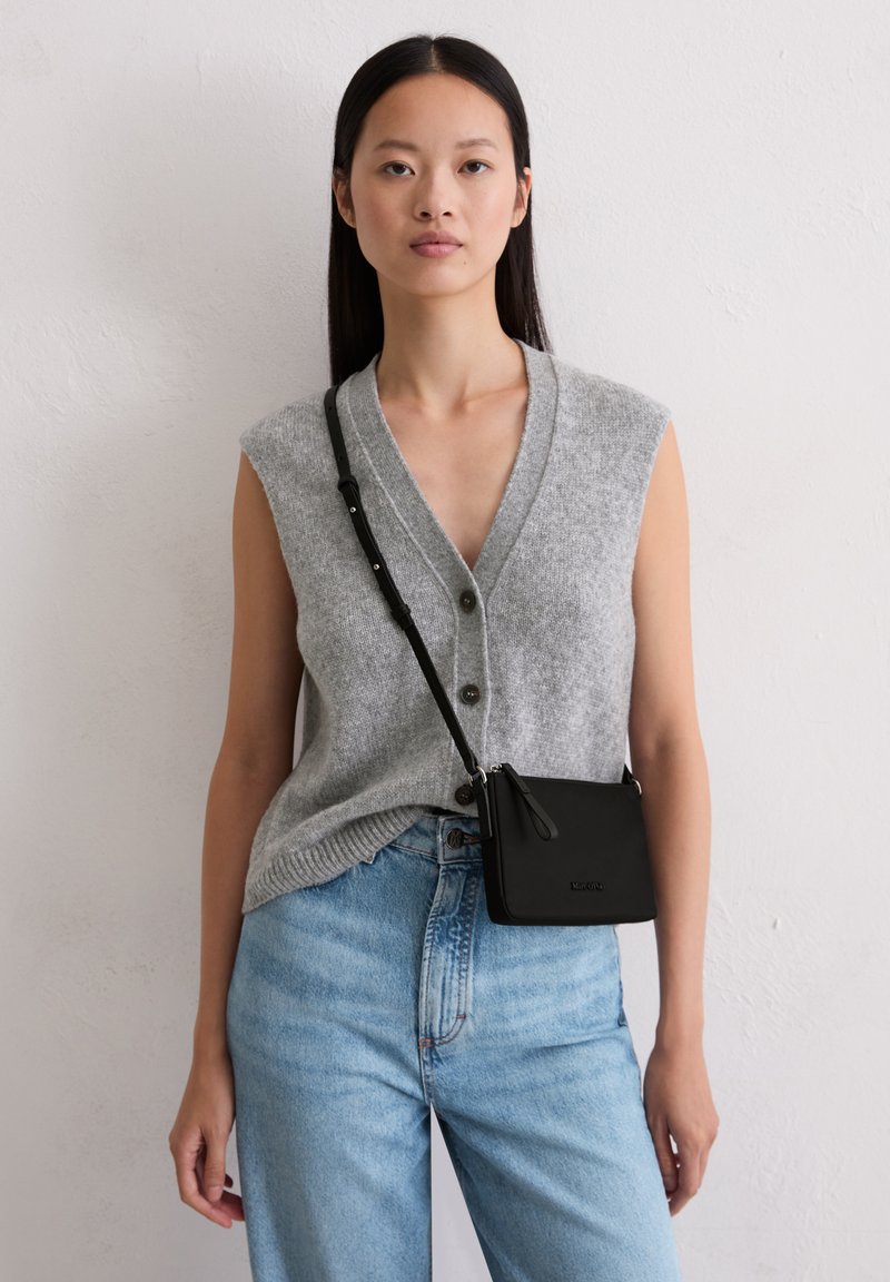 Cardigan senza maniche grigio in lana con scollatura a V e bottoni abbinato a jeans in denim blu chiaro a vita alta e una piccola borsa a tracolla nera.