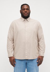 Camicia button-up beige chiaro con colletto e maniche lunghe, realizzata in un tessuto texturizzato. Presenta chiusure a bottoni e una vestibilità morbida.