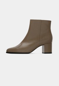 Braune Leder-Ankle Boots mit glatter Oberfläche, abgerundeter Zehe und einem klobigen, quadratischen Absatz. Minimalistisches Design mit klaren Linien.