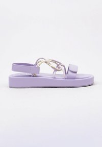 Sandalias planas de lavanda con un acabado suave, que presentan una amplia tira en la parte delantera, un tacón curvado y detalles laterales trenzados de múltiples colores.