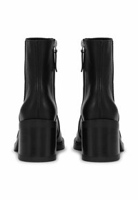 Crne gležnjače od kože s glatkim završetkom, patentnim zatvaračem i blok petom. Imaju šavove duž ruba.