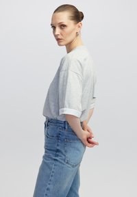 Grijze, korte mouw t-shirt met opgerolde mouwen, gecombineerd met hooggesneden blauwe denim jeans met een klassieke snit en achterzakken.