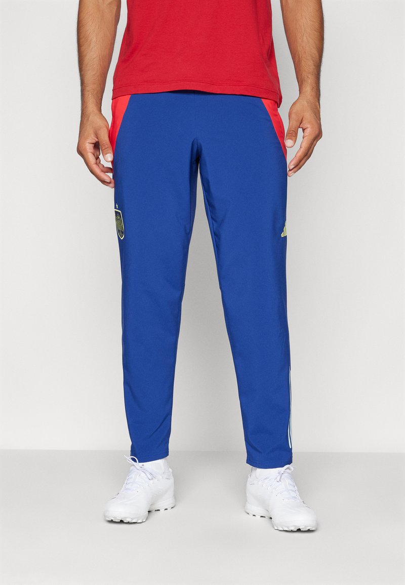 Pantalones deportivos azules con paneles laterales rojos. Presenta un logo bordado en la pierna izquierda y franjas blancas a lo largo de los lados. Hechos de material ligero.
