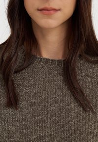 Pull marron tricoté avec une surface texturée, doté d'un col rond et de bords côtelés, partiellement caché par des cheveux lâches brun foncé.