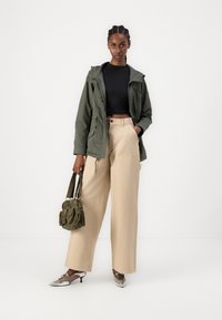 Veste à capuche olive, crop top noir, pantalon large beige, sac olive avec poches et escarpins argentés à bout pointu.